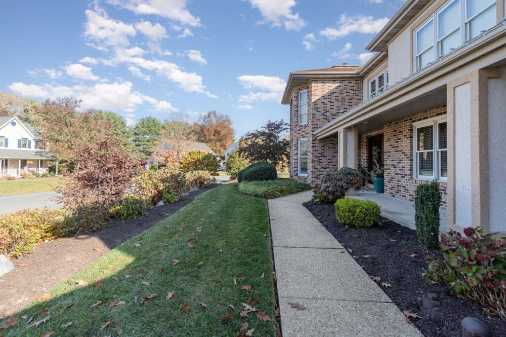 A side view of a home, with green grass and leaves on the lawn